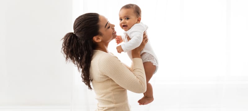 Young Black Mother Holding Baby Toddler Standing Near Window Indoor